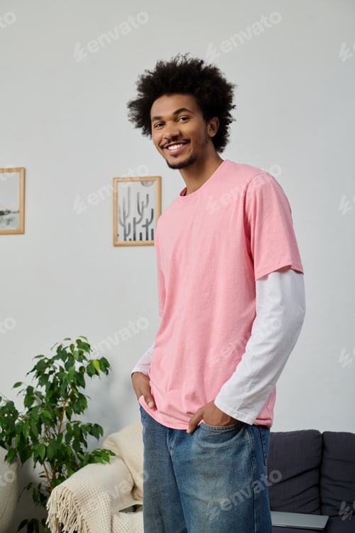 Preview: Young handsome man poses cheerfully in a cozy indoor setting wearing a stylish pink shirt