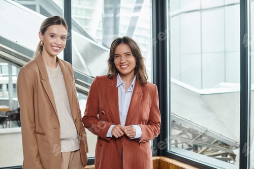 Preview: two female colleagues in stylish formal attire posing on window background, coworking concept
