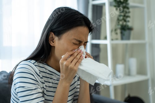 Preview: Asian beautiful woman having running nose and sneezing in living room. A