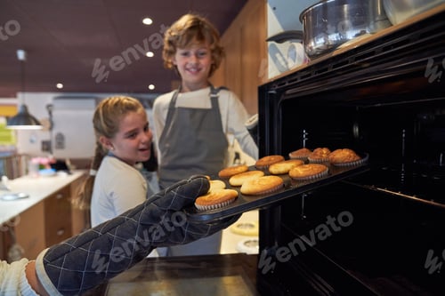 Preview: Faceless person taking cupcakes from oven near children