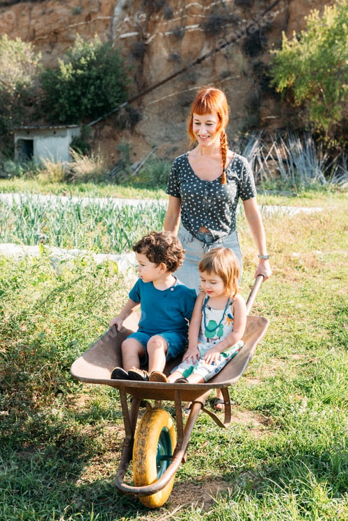 Preview: Mother Enjoys Outdoor Time Carrying Kids in a Wheelbarrow Through a Green Garden