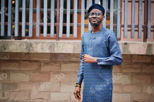 Preview: African guy in blue authentic costume, eyeglasses and beret. Fashionable nigerian man.