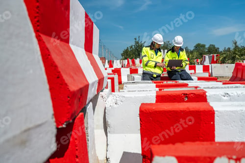 Preview: Two engineers sit amidst red-and white barricades at a construction site.