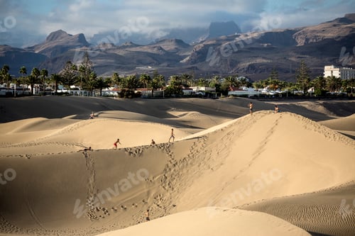 Preview: Travelers exploring vast sand dunes against a backdrop of mountainous terrain and a clear sky.
