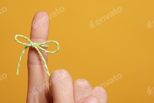 Preview: Woman showing index finger with tied bow as reminder on orange background, closeup. Space for text