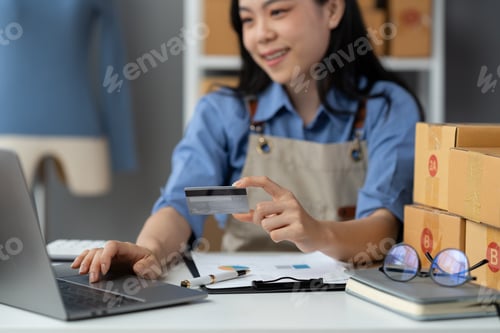 Preview: Self-employed business owner holding credit card sits working with laptop to conduct financial busin