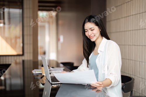 Preview: Professional woman analyzing documents and working on a laptop in a modern office setting.