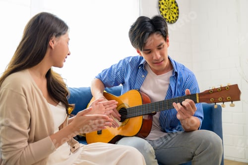Preview: Couple of man and woman playing guitar together at home on weekend, Happy people enjoying and