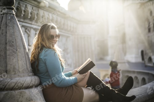 Preview: Young attractive Hispanic girl sitting outdoors reading a book