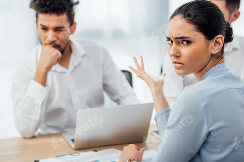 Preview: Selective focus of skeptical mexican businesswoman looking at camera near african american colleague