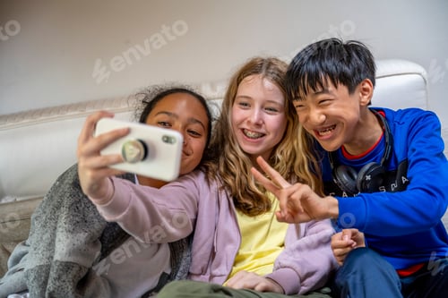 Preview: Three cheerful kids taking a selfie on a couch, with one flashing a peace sign.