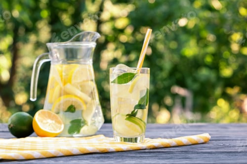 Preview: Lemonade in jug and glass and lemon with lime on wooden table