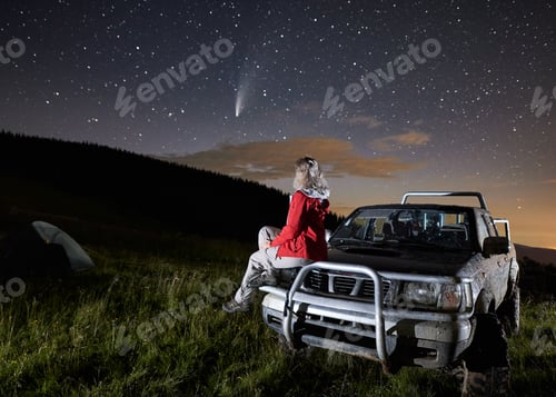 Preview: Woman sitting on car hood and watching starry sky.