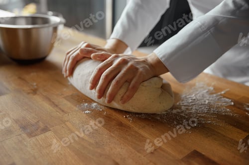 Preview: Woman baker wearing uniform kneading dough at kitchen