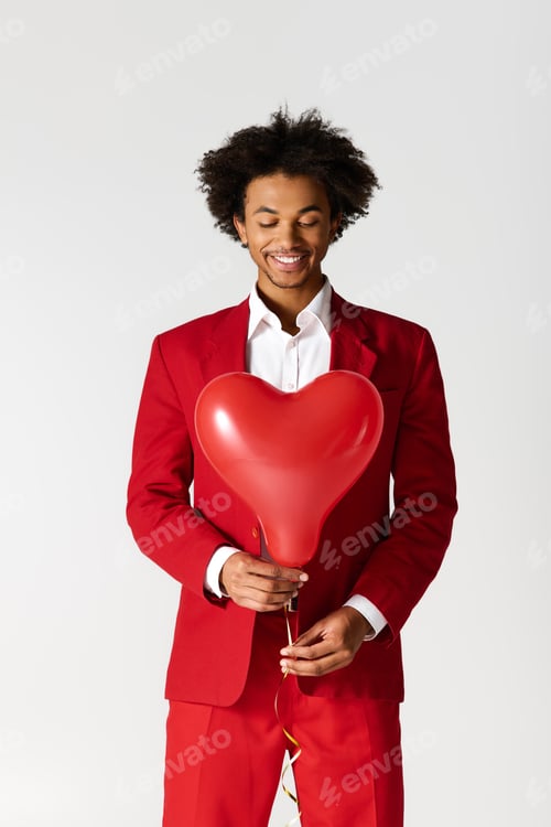 Preview: Charming young man in red suit holds heart shaped balloon with a joyful smile