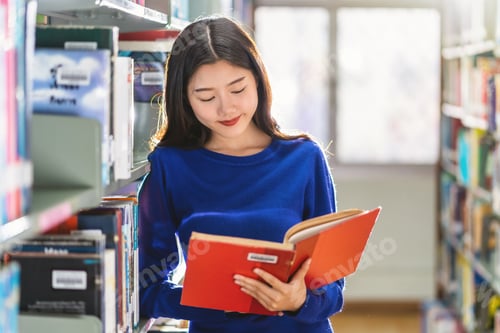 Preview: Asian young Student in casual suit standing and reading the book at book shelf in library