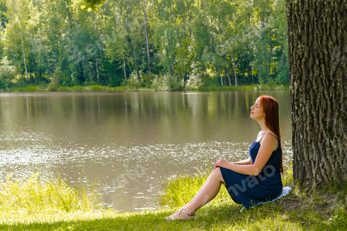 Preview: woman sitting under high big oak,trunk tree lake,river,meditating,relaxing.girl,nature landscape
