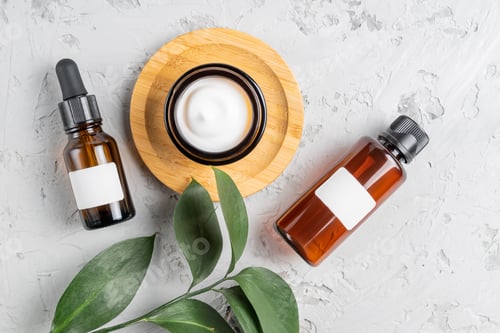Preview: Moisturizer cream jar, serum in glass bottle and toner with green leaves on concrete background.