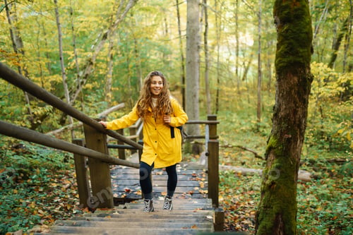 Preview: Woman in a yellow coat with backpack walks along wooden staircase, enjoying autumn scenery in forest