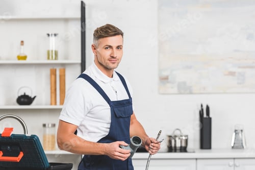 Preview: adult repairman holding pipes for kitchen faucet repairing and looking at camera
