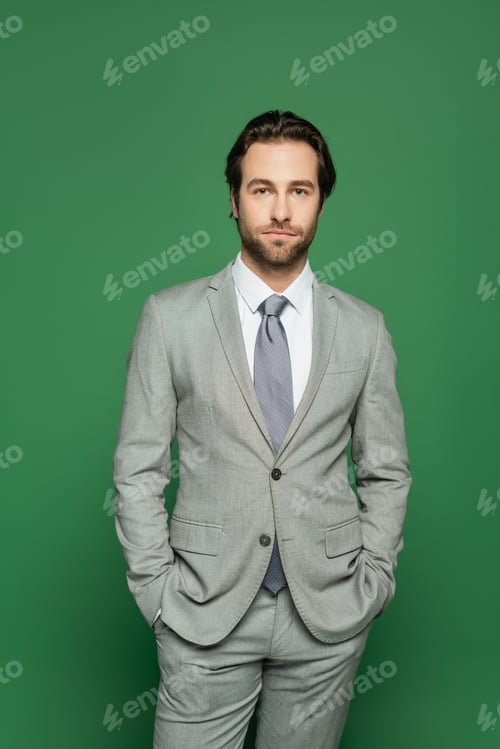 Preview: Brunette newscaster in suit holding hands in pockets isolated on green