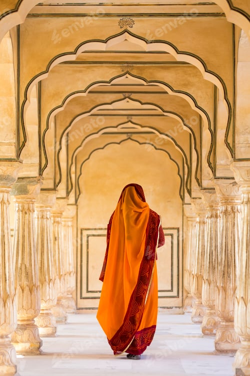 Preview: Rear view of woman wearing orange sari walking along a colonnade.