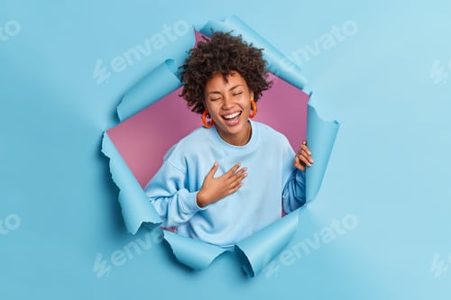 Preview: Optimistic joyful dark skinned young ethnic woman laughs out cannot stop giggling keeps hand on ches
