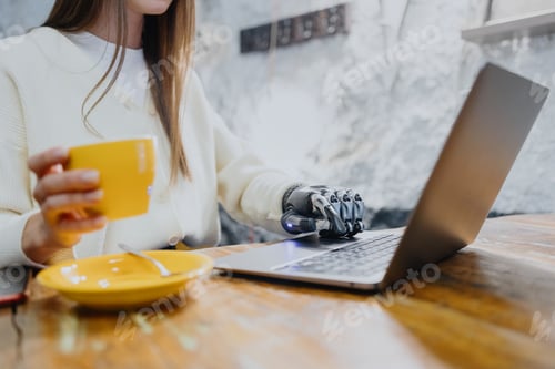 Preview: woman with a bionic prosthetic arm is working on a laptop and drinking coffee in a coffee shop