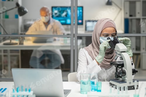 Preview: Young Muslim female virologist studying new virus in microscope in laboratory