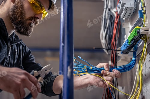 Preview: A male electrician works in a switchboard with an electrical connecting cable.
