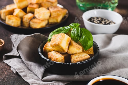 Preview: Fried vegetarian tofu cheese cubes and basil leaves in bowl on table
