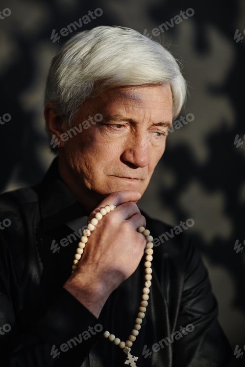 Preview: Vertical white haired senior priest holding rosary deep in thought
