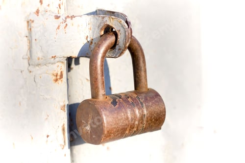 Preview: Close-up of lit by sun old rough metal padlock on garage or barn iron gate. Outdated technology