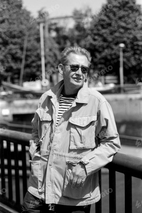 Preview: Senior man wearing sunglasses and light jacket leaning on railing in black and white