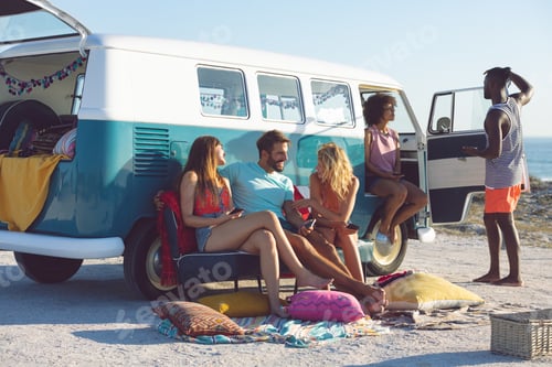 Preview: Front view of young group of diverse friends interacting with each other near camper van at beach