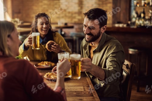 Preview: Happy man and his friends toasting with beer while eating in a pub.