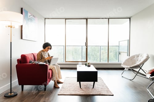 Preview: Modern smiling curly business woman, freelancer holding mobile phone, using laptop