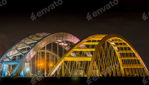 Preview: Bridges in a city with large yellow and white arches on top at nighttime