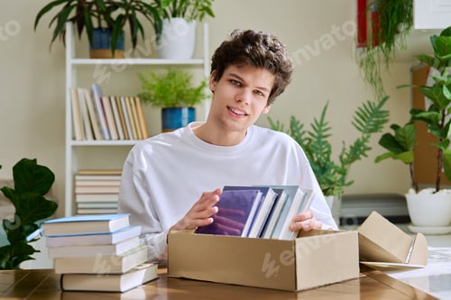 Preview: Satisfied young male customer unpacking cardboard box with online purchases, new books