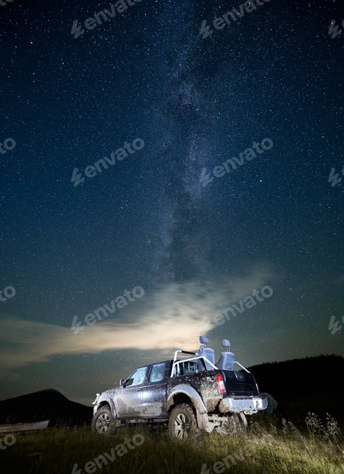Preview: Illuminated pickup offroad truck in mud on mountain meadow at night under starry sky
