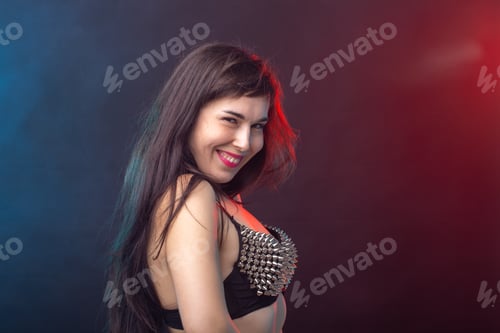 Preview: Beautiful young sexy brunette woman posing on a dark background in a riveted top on a dark