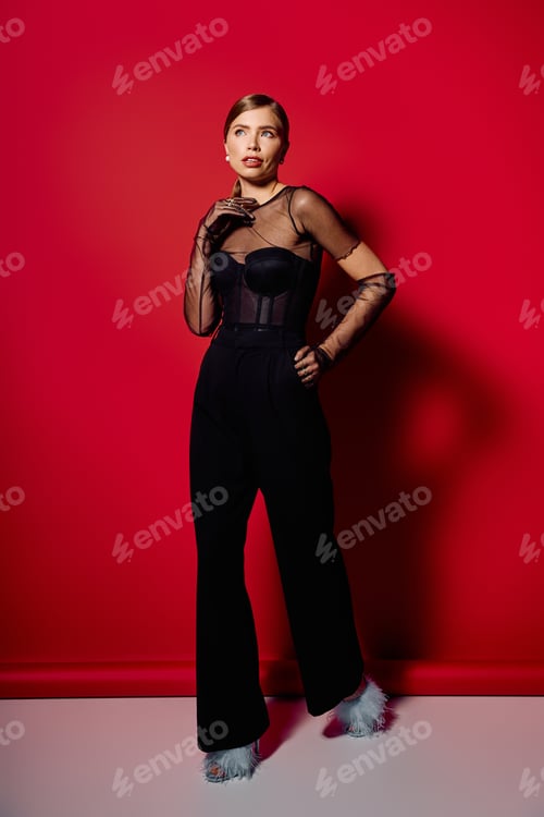 Preview: Elegant woman in a stylish black outfit poses against a vibrant red backdrop