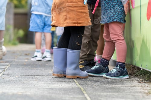 Preview: Children lined up against a colorful fence, showcasing a variety of footwear and playful attire.