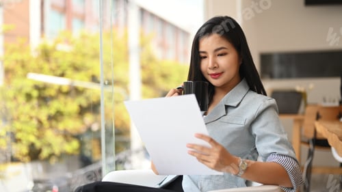 Preview: Attractive asian female manager sitting near large window in modern office.