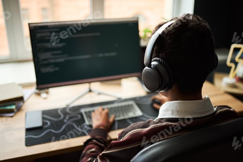 Preview: Young Adult Man Coding on Computer While Wearing Headphones in Office
