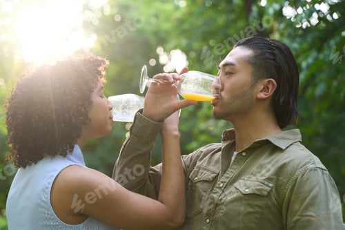 Preview: Interracial couple drinking juice in nature during sunset
