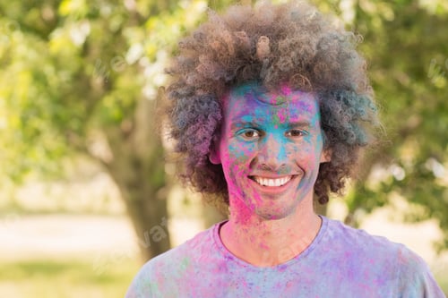 Preview: Curly-haired adult man grinning while standing in park with powder-covered T-shirt and face