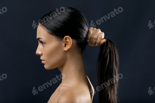 Preview: Side view of a woman holding her black hair