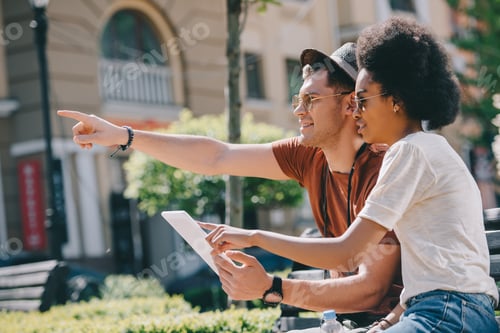 Preview: young male traveler pointing by finger to african american girlfriend with digital tablet