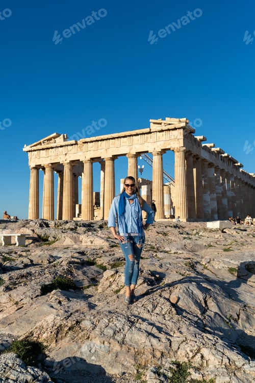 Preview: Vertical shot of a Caucasian blonde woman posing in front of Acropolis, Athens